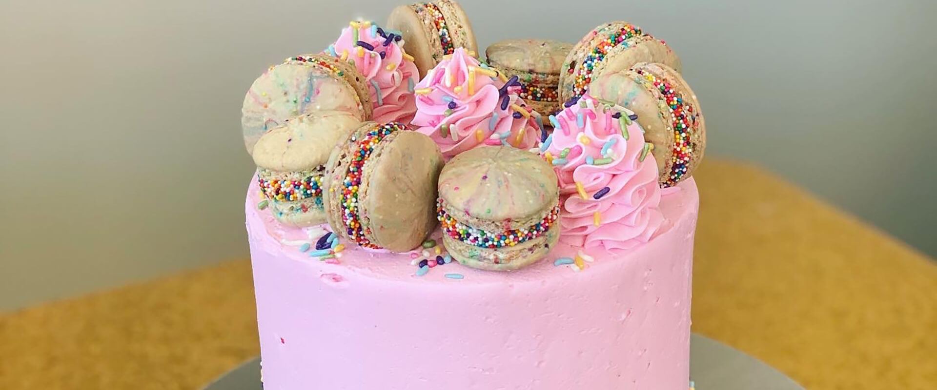 Pink buttercream cake topped with macarons and sprinkles