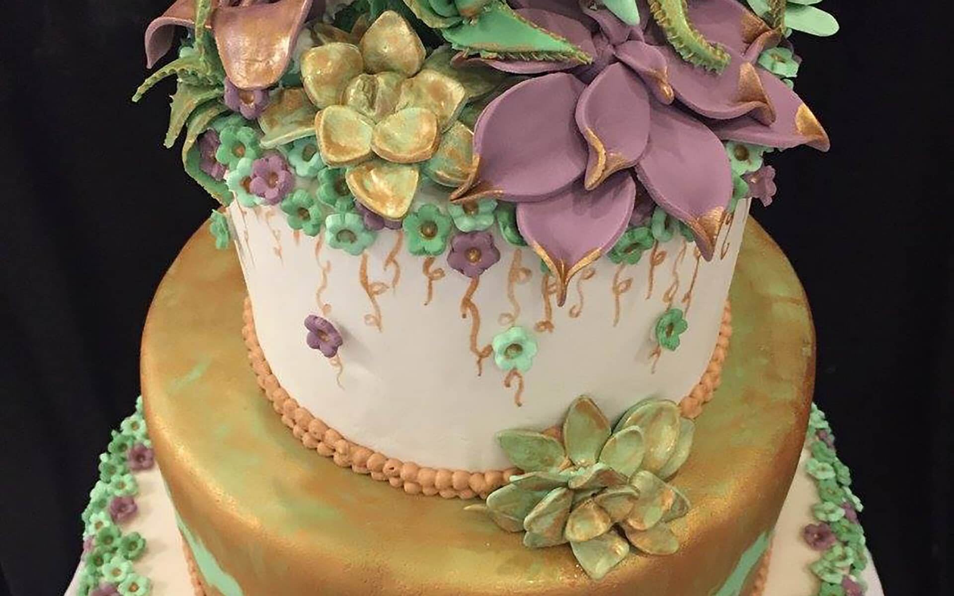Tiered gold and white cake finished with sugar succulents and magnolia flowers