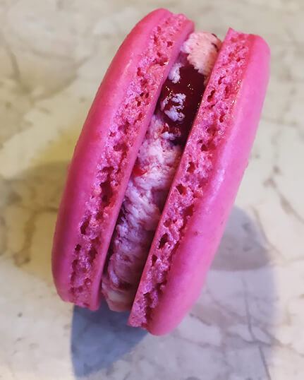 Single raspberry macaron, gluten-free by recipe, on a marble surface